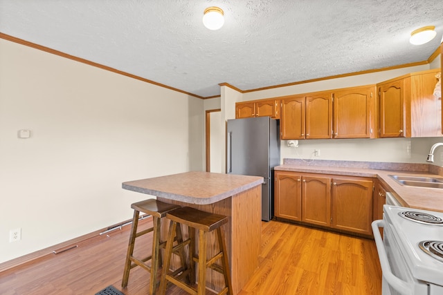 kitchen featuring sink, white electric range, stainless steel fridge, a breakfast bar area, and light wood-type flooring