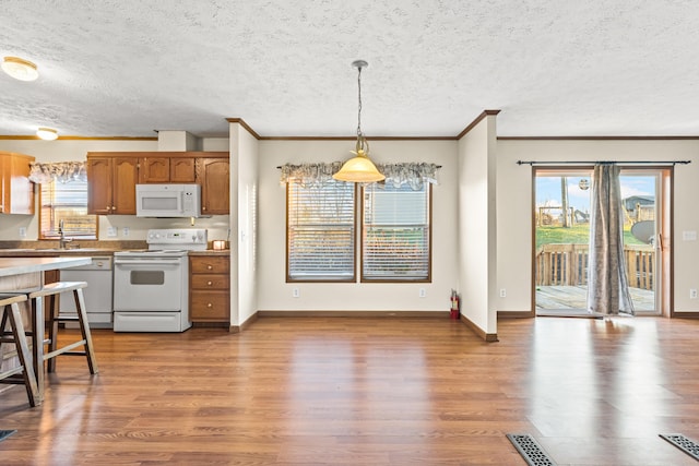 kitchen featuring pendant lighting, hardwood / wood-style floors, white appliances, and crown molding