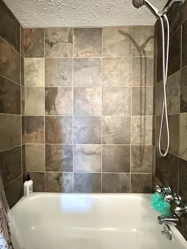 bathroom with a textured ceiling and tiled shower / bath