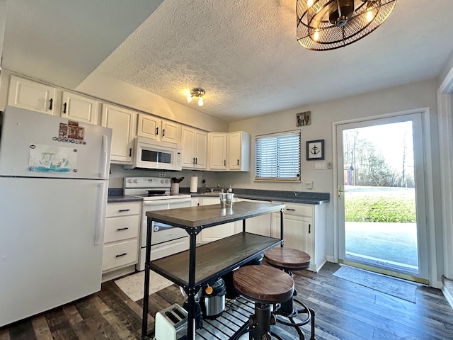 kitchen with white cabinets, dark hardwood / wood-style flooring, white appliances, and a textured ceiling