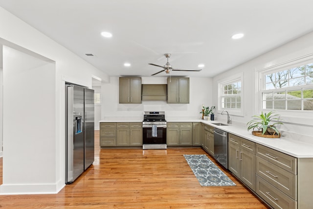 kitchen with exhaust hood, sink, light wood-type flooring, and appliances with stainless steel finishes