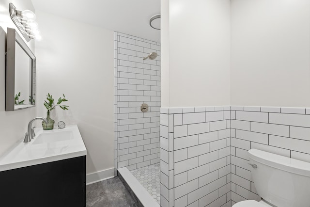 bathroom featuring vanity, toilet, tiled shower, and tile walls