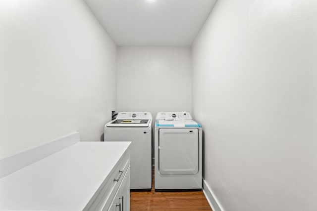 washroom featuring hardwood / wood-style floors, cabinets, and washing machine and clothes dryer