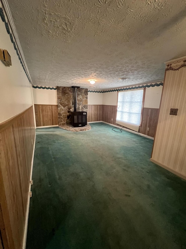 interior space featuring dark colored carpet, wood walls, a wood stove, and a textured ceiling