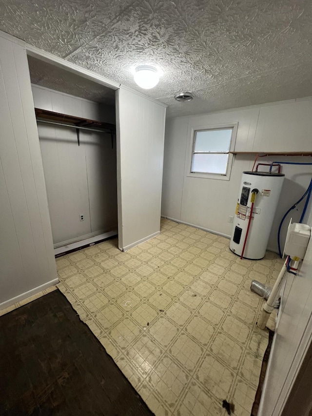 basement featuring baseboard heating, electric water heater, and a textured ceiling