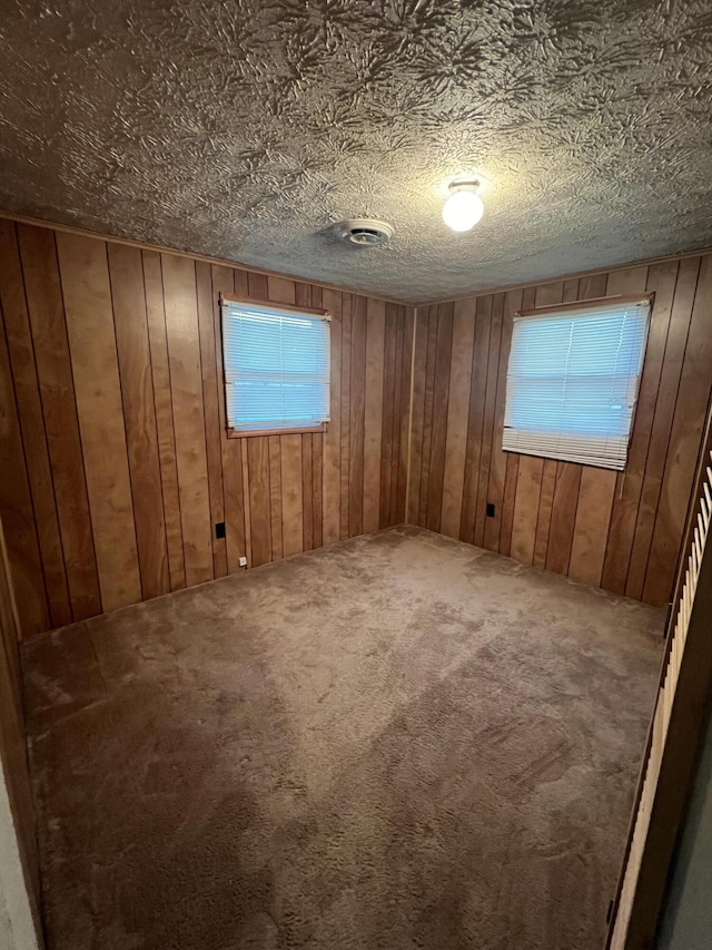 carpeted spare room featuring wooden walls and a textured ceiling