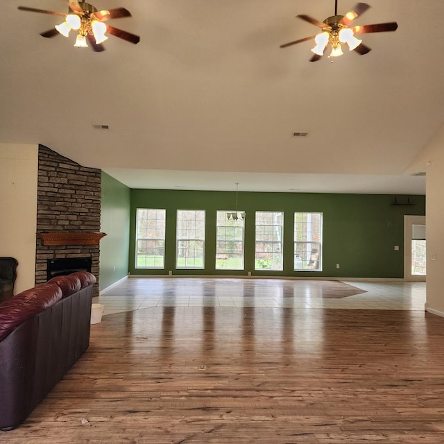 living room featuring ceiling fan, a stone fireplace, light wood-type flooring, and high vaulted ceiling