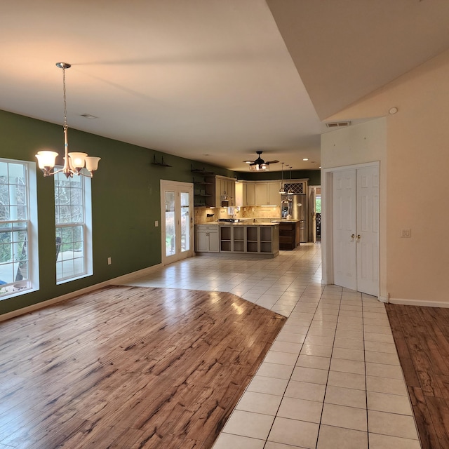 unfurnished living room with ceiling fan with notable chandelier and light wood-type flooring