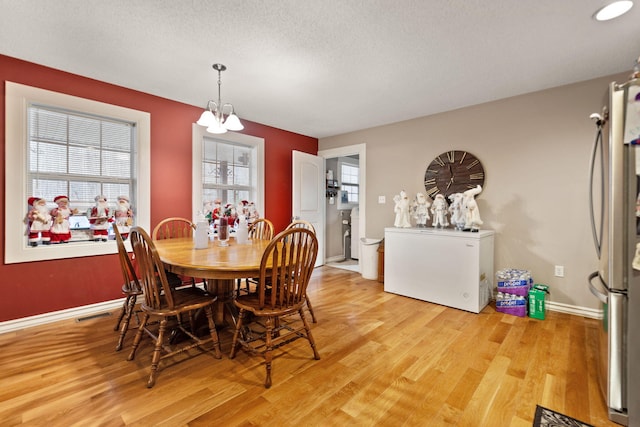 dining area with light hardwood / wood-style floors, a textured ceiling, and a chandelier