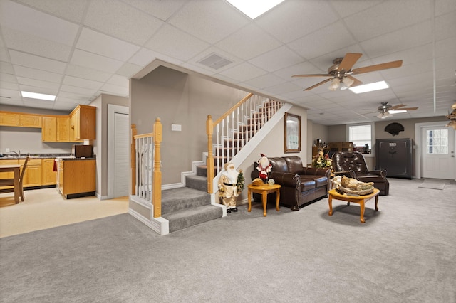 living room featuring a paneled ceiling, light colored carpet, and ceiling fan