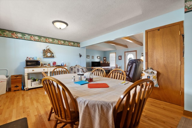 dining room with beam ceiling, light hardwood / wood-style floors, and a textured ceiling