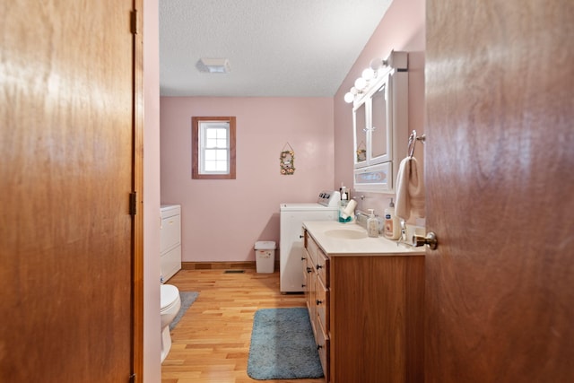 bathroom featuring vanity, hardwood / wood-style flooring, toilet, washing machine and dryer, and a textured ceiling