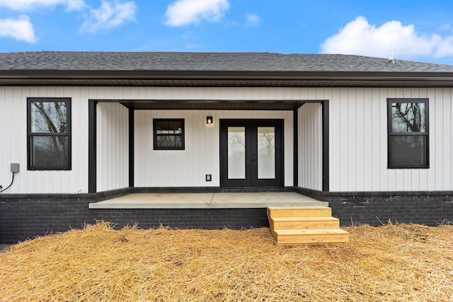 doorway to property with a shingled roof, french doors, and brick siding