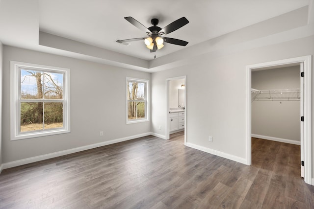 unfurnished bedroom with a closet, dark wood finished floors, a walk in closet, and baseboards