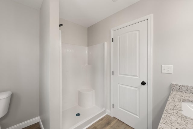 bathroom featuring a walk in shower, wood finished floors, toilet, and baseboards