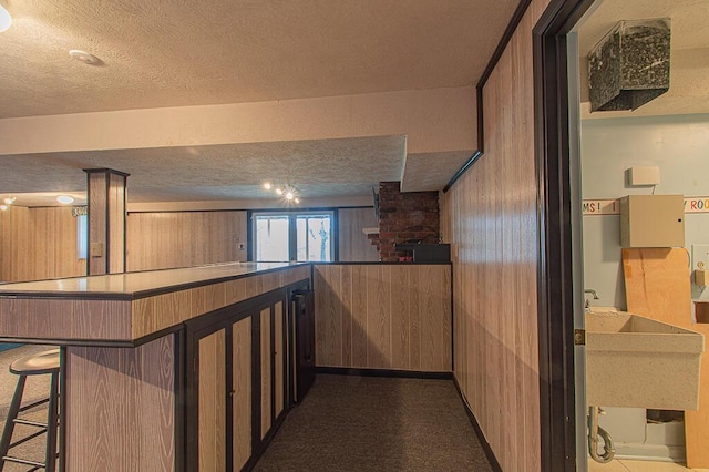 interior space featuring kitchen peninsula, a textured ceiling, a breakfast bar area, and wood walls