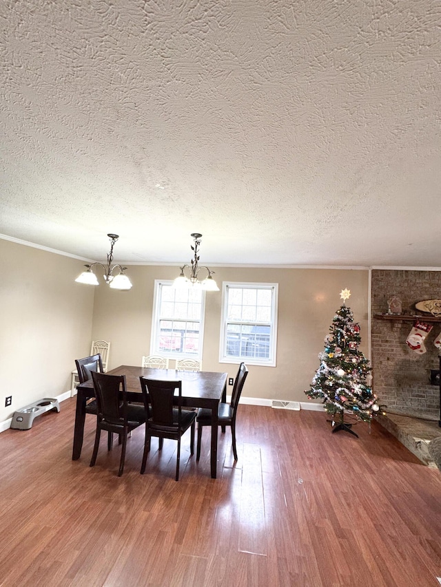 dining space with a textured ceiling, hardwood / wood-style flooring, an inviting chandelier, and ornamental molding