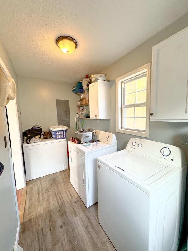 laundry area featuring cabinets, light wood-type flooring, a textured ceiling, washer and clothes dryer, and electric panel