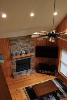 living room featuring vaulted ceiling, ceiling fan, wood-type flooring, a stone fireplace, and wood walls