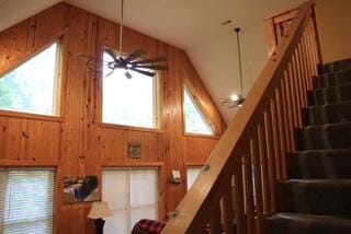 stairway featuring ceiling fan, wood walls, and high vaulted ceiling