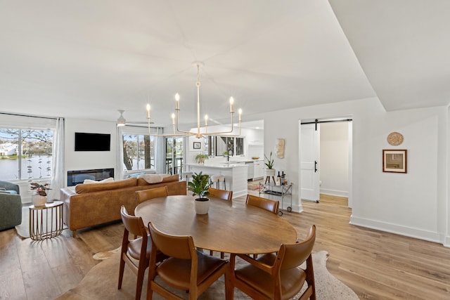 dining room with a barn door, sink, an inviting chandelier, and light wood-type flooring