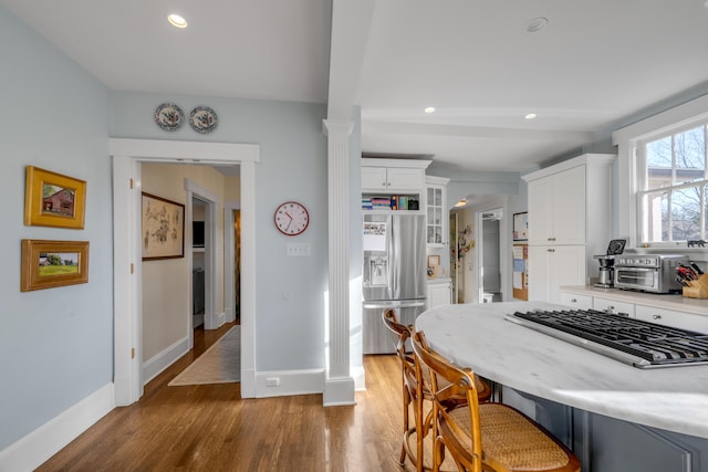 kitchen featuring appliances with stainless steel finishes, light wood-type flooring, ornate columns, a breakfast bar, and white cabinetry