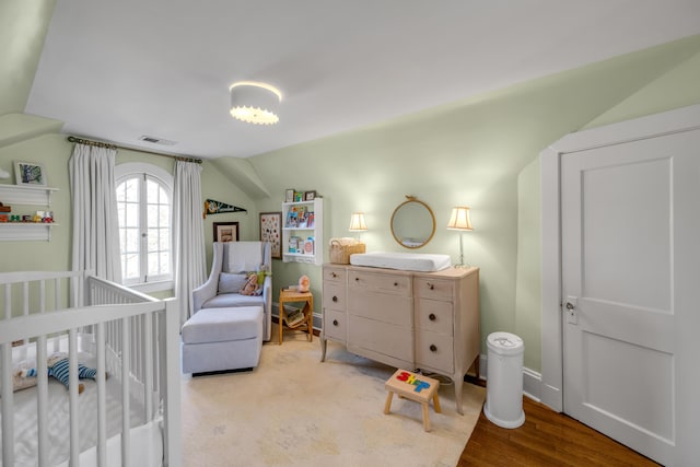 bedroom featuring a crib, wood-type flooring, and vaulted ceiling