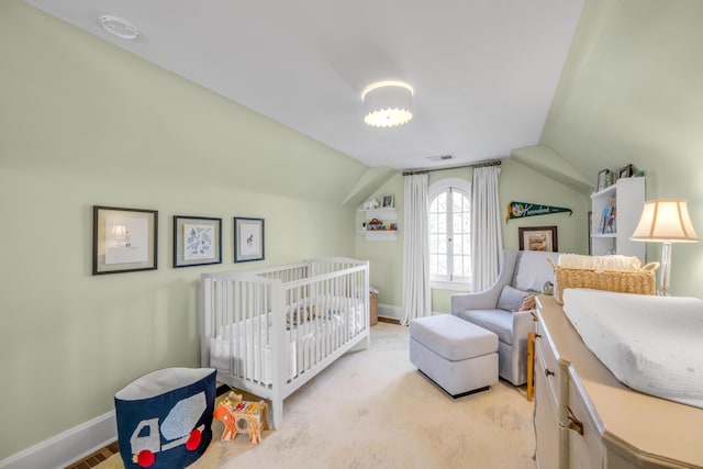 bedroom featuring lofted ceiling, a crib, and light carpet