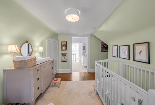 bedroom with a nursery area, vaulted ceiling, and light wood-type flooring