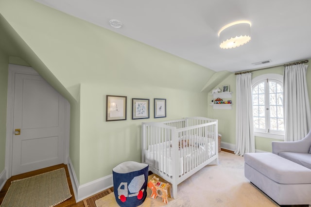 bedroom featuring vaulted ceiling, light hardwood / wood-style floors, and a nursery area