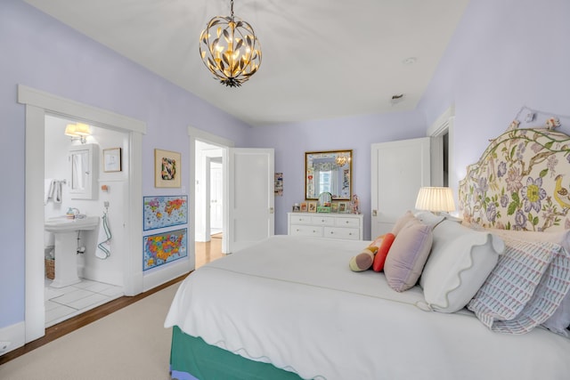 bedroom featuring a chandelier, hardwood / wood-style floors, ensuite bathroom, and sink