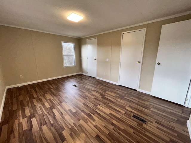 unfurnished bedroom featuring a textured ceiling, dark hardwood / wood-style flooring, two closets, and ornamental molding