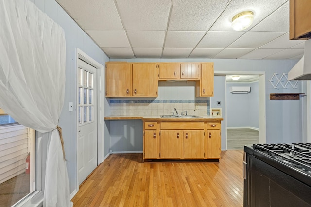 kitchen with a drop ceiling, black range with gas stovetop, an AC wall unit, decorative backsplash, and light wood-type flooring