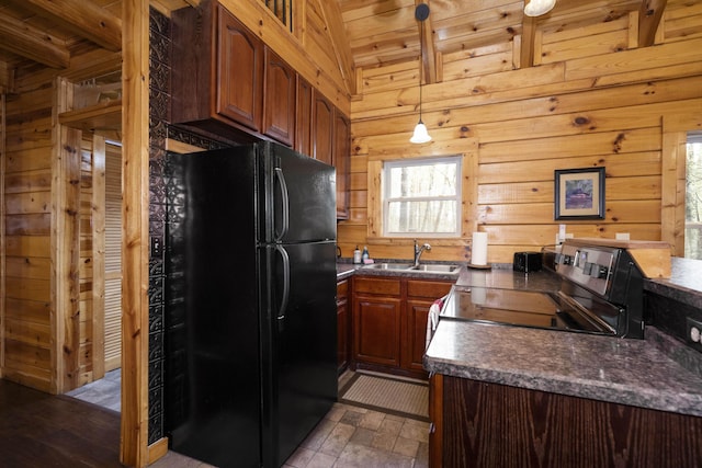 kitchen featuring black fridge, sink, hanging light fixtures, stainless steel range with electric cooktop, and wood walls