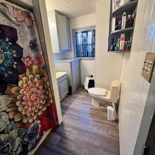 full bathroom with a textured ceiling, wood finished floors, toilet, and a shower with curtain