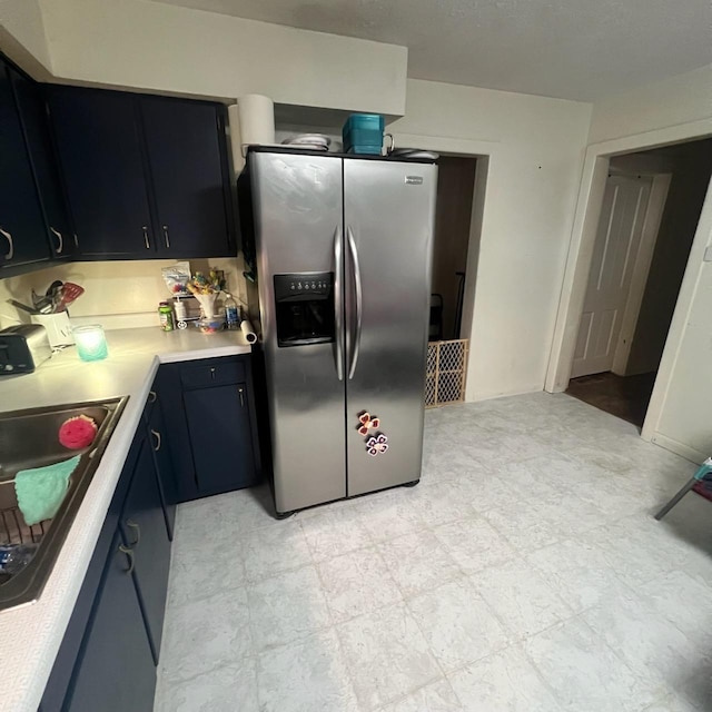 kitchen with light countertops, dark cabinetry, light floors, stainless steel refrigerator with ice dispenser, and a sink