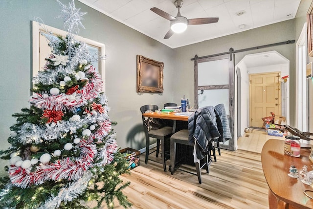 dining room with a barn door, hardwood / wood-style flooring, and ceiling fan