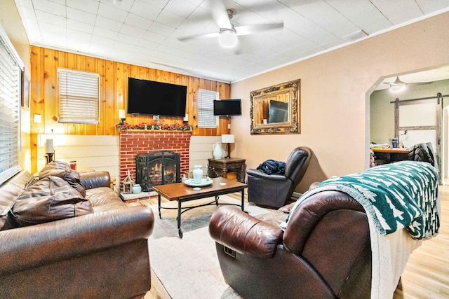 living room featuring ceiling fan, a brick fireplace, hardwood / wood-style floors, wooden walls, and ornamental molding