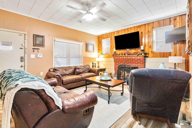 living room featuring ceiling fan, wood walls, a fireplace, and light hardwood / wood-style flooring