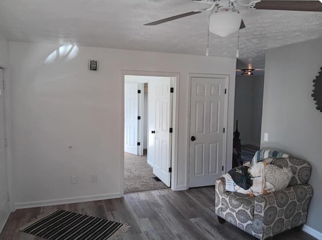 living area featuring ceiling fan, dark wood-type flooring, and a textured ceiling