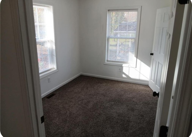 empty room featuring carpet flooring, baseboards, visible vents, and a healthy amount of sunlight