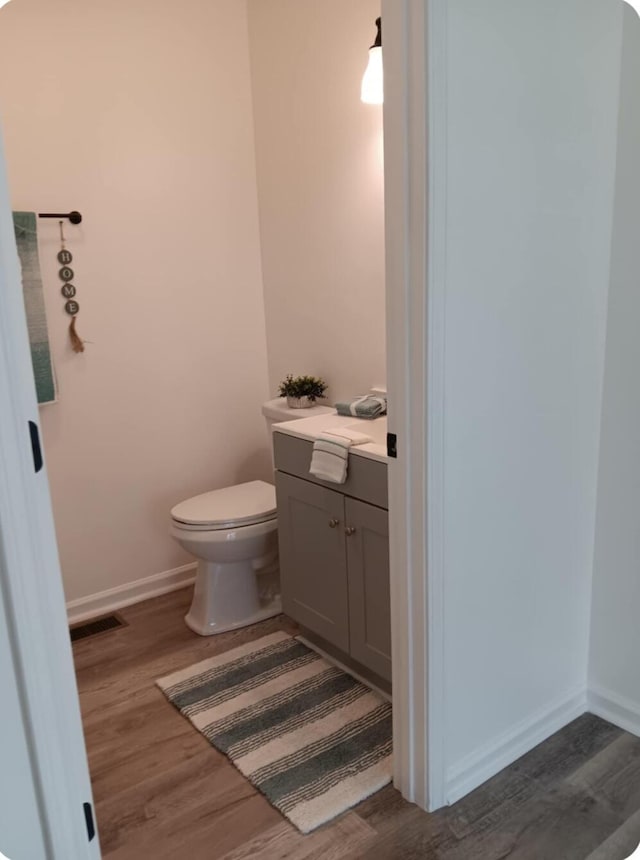 half bath with toilet, baseboards, visible vents, and wood finished floors