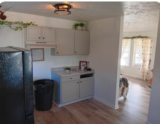 kitchen featuring black refrigerator, a textured ceiling, and light wood-type flooring