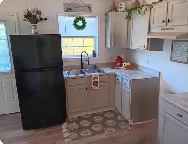 kitchen with white cabinetry, black fridge, sink, and light hardwood / wood-style floors