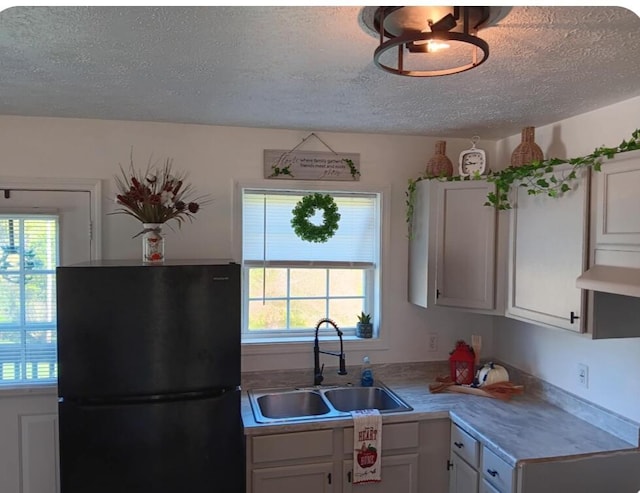 kitchen featuring a sink, light countertops, a textured ceiling, freestanding refrigerator, and white cabinetry