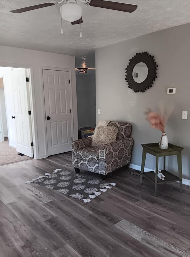 living area featuring ceiling fan, dark wood-type flooring, and a textured ceiling