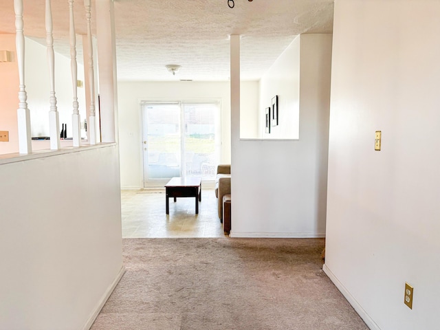 hallway featuring light colored carpet and a textured ceiling