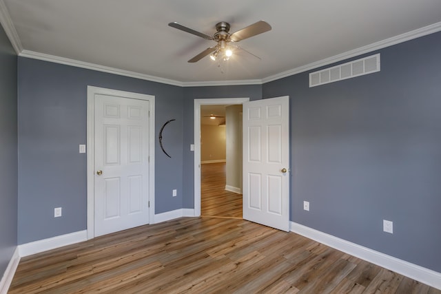 empty room with baseboards, light wood finished floors, visible vents, and crown molding