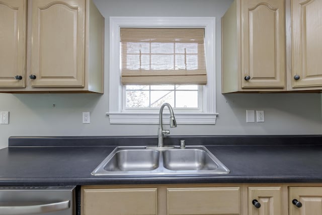 kitchen featuring dark countertops, stainless steel dishwasher, a sink, and light brown cabinetry