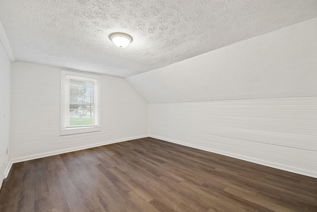 additional living space featuring dark hardwood / wood-style flooring, lofted ceiling, and a textured ceiling